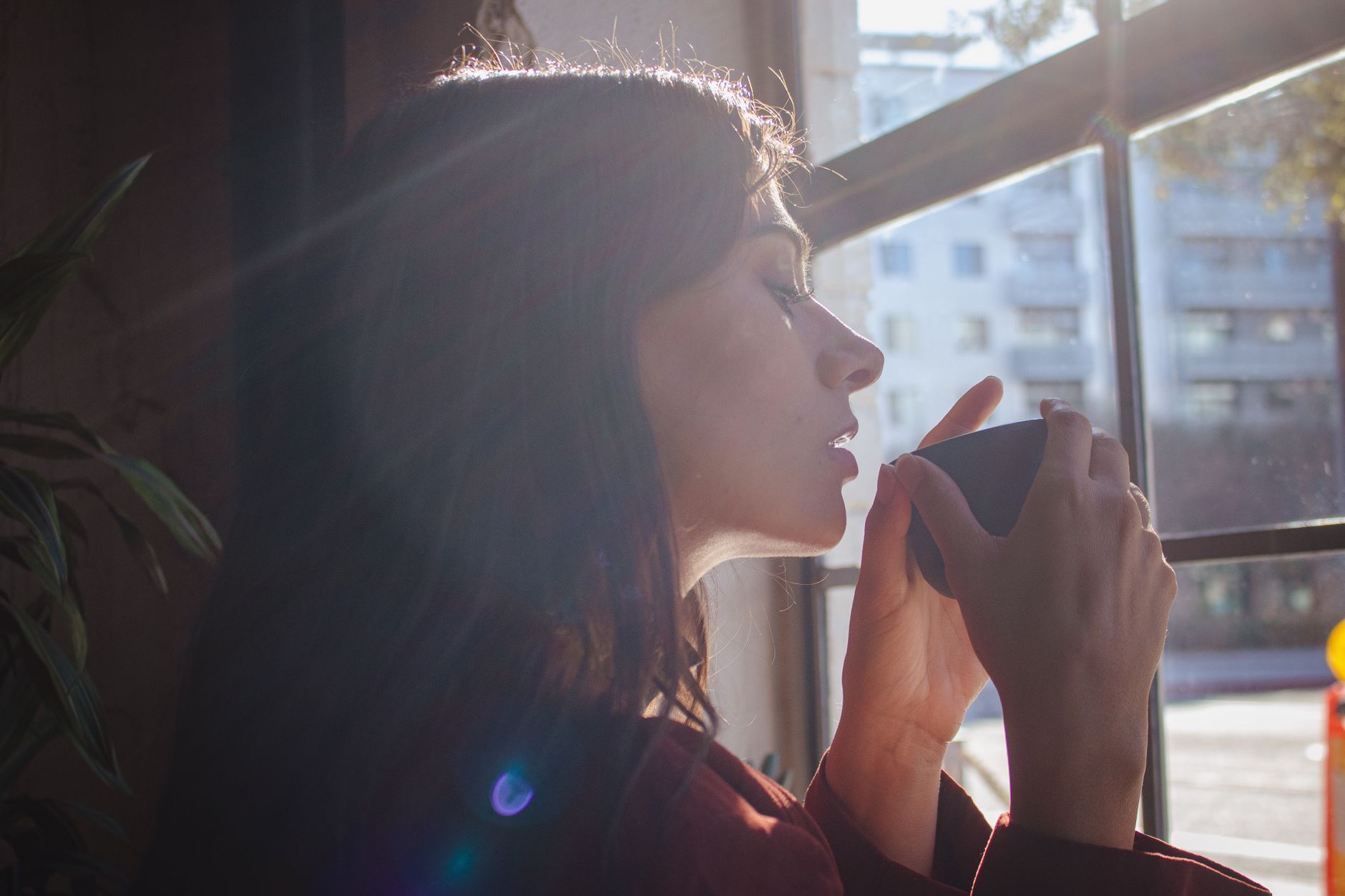 Mujer tomando una bebida caliente junto a una ventana con luz natural por la mañana