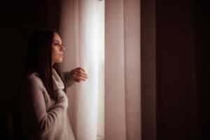 Mujer mirando pensativa por la ventana en luz cálida de la mañana