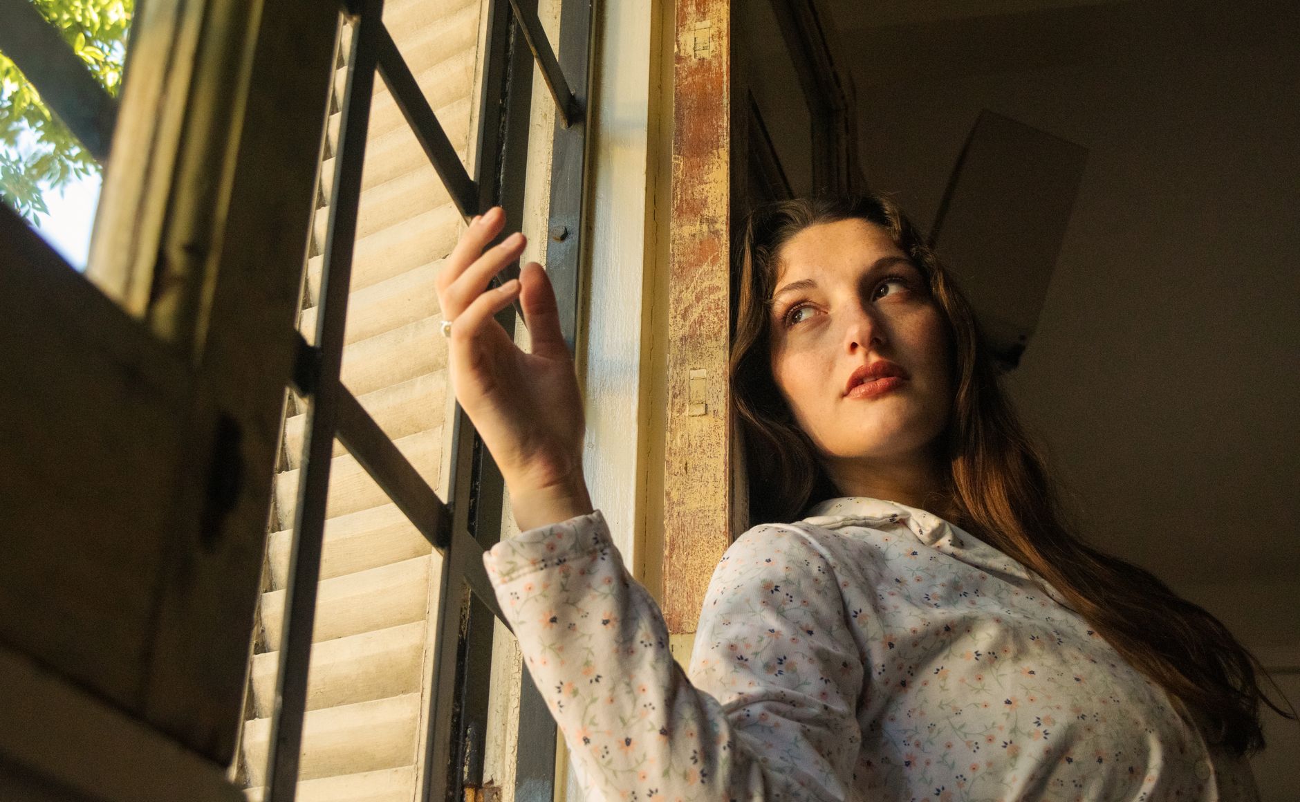 Mujer mirando pensativa a través de una ventana con luz cálida