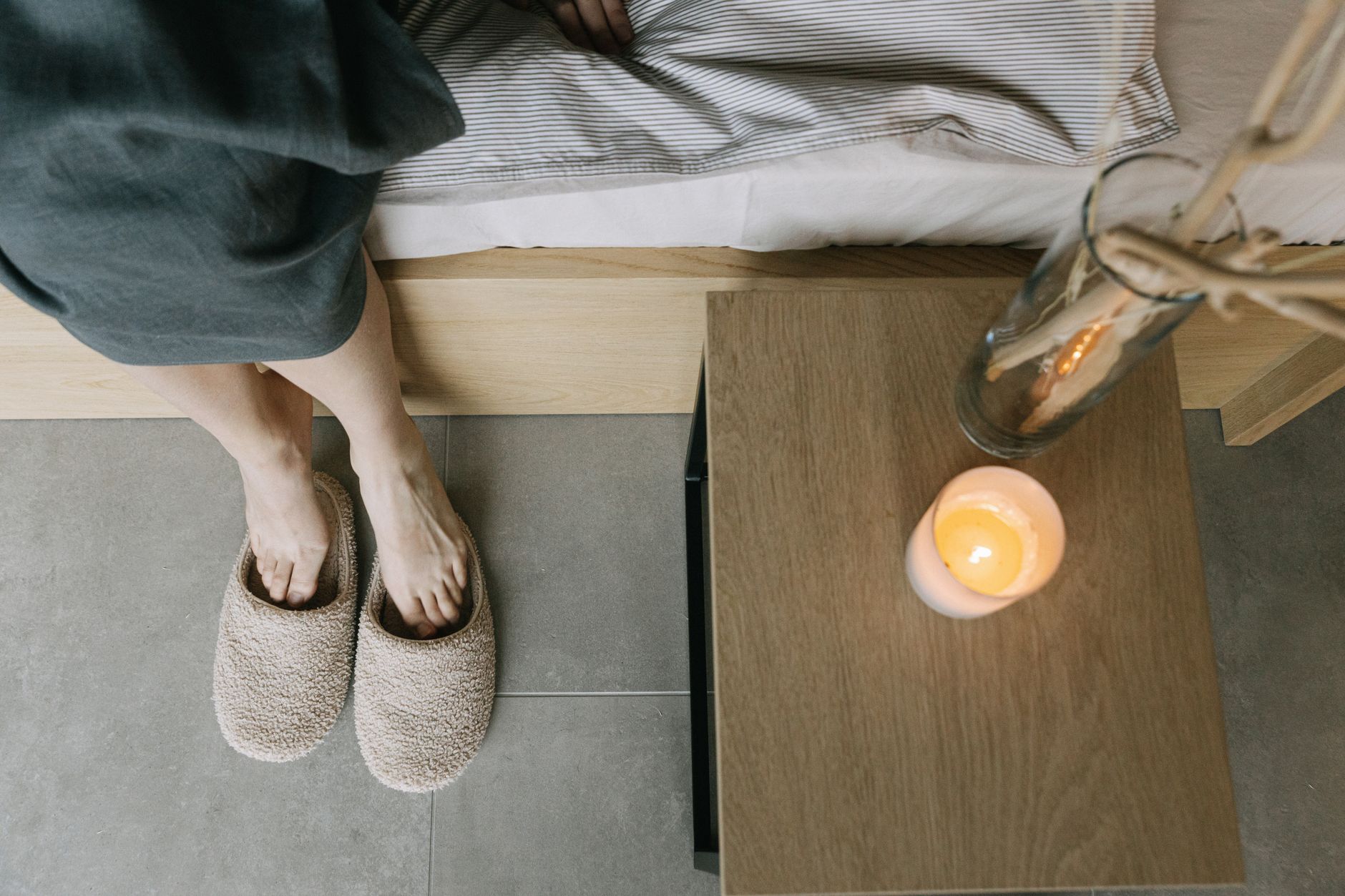 Pies descalzos apoyados en el suelo al borde de una cama, luz suave de mañana