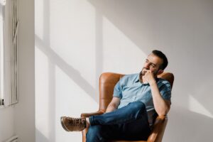 Hombre sentado pensativo en un sillón junto a una ventana con luz natural
